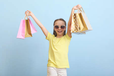 Beautiful smiling little girl with bags for shopping on a colored background.の写真素材