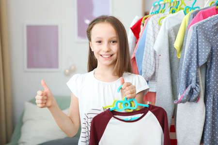 Cute cheerful little girl chooses clothes with floor hangers.の写真素材