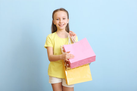Beautiful smiling little girl with bags for shopping on a colored background.の写真素材