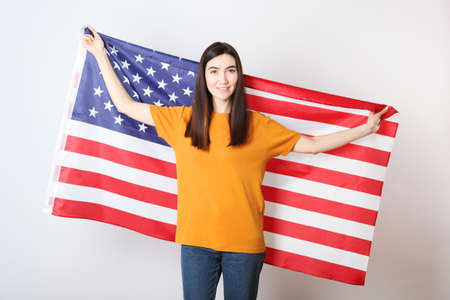 Beautiful young girl holding the flag of America on a colored background.