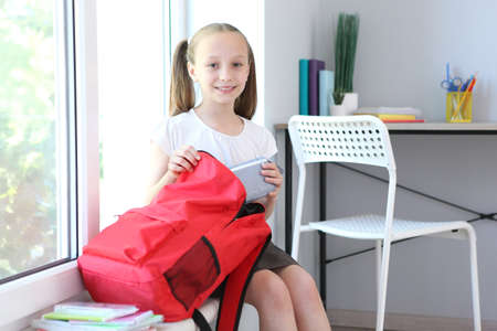 Cute cheerful schoolgirl puts stationery in a backpack.の写真素材