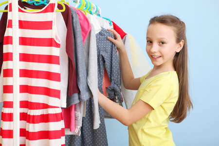 Cute cheerful little girl chooses clothes with floor hangers.の写真素材