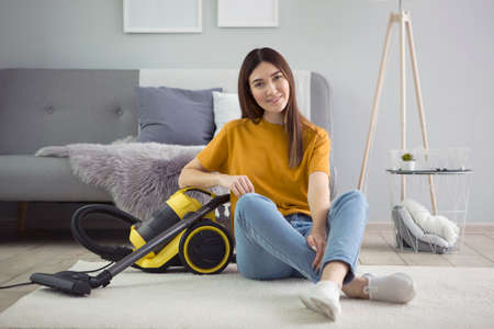 Beautiful young girl in a good mood makes house cleaning with a vacuum cleanerの写真素材