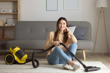Beautiful young girl in a good mood makes house cleaning with a vacuum cleanerの写真素材