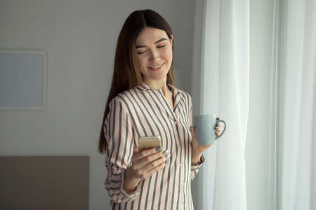 Beautiful young girl in a good mood in pajamas in the bedroomの写真素材