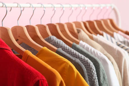 fashionable clothes on hangers on a wardrobe rack on a colored background.の写真素材