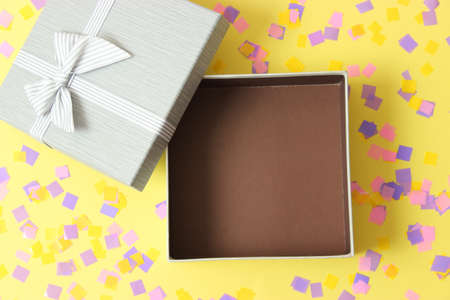 open gift box and confetti on a colored background top view.