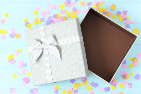 open gift box and confetti on a colored background top view.