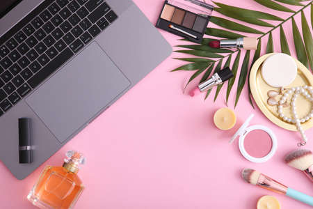 Makeup cosmetics and modern laptop on a colored background top view.
