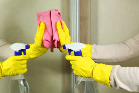 Woman in gloves wipes the mirror with detergents close-upの写真素材