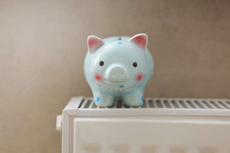 Pig piggy bank on a radiator indoors close-up. Heating concept.の写真素材