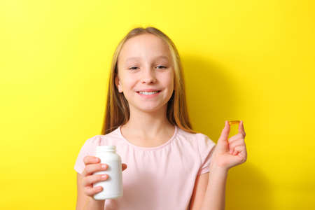 A teenage girl holds an omega 3 capsule in her hands on a colored background.の写真素材
