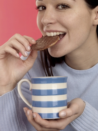Young Woman Dipping Biscuit Into Hot Drink. Model Releasedの写真素材