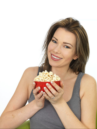 Attractive Happy Young Caucasian Woman Eating and Enjoying a Bowl of Popcorn Wearing A Grey Vest Top Shot Against Whiteの写真素材