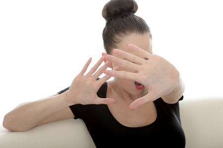 Portrait Of A Beautiful Attractive Young Caucasian Woman Posing On A Sofa Or Couch Fending Off Looking Scared anf Frightened Holding Hand Up In Defenceの写真素材