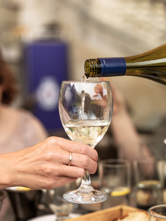 Pouring White Wine into a Glass Held by a Hand in Close Up Against a Table Settingの写真素材