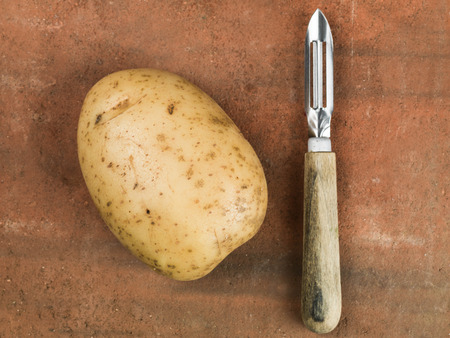 Single Uncooked Raw King Edward Potato With a Vegetable Peelerの写真素材