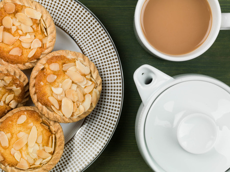 Bakewell Tarts With a Teapot and a Mug of Tea On A Green Backgroundの写真素材