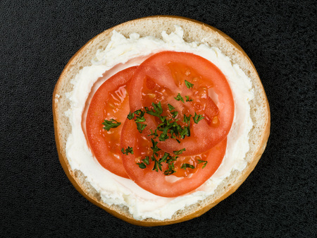 Bagel With Cream Cheese and Tomato Against a Black Backgroundの写真素材