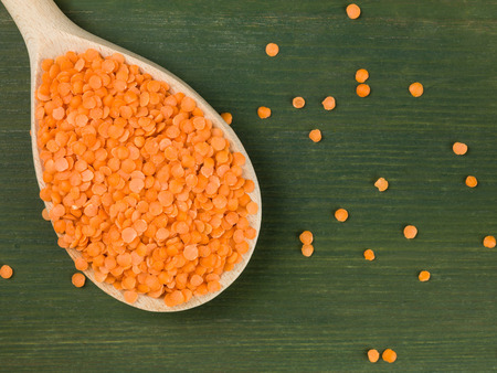 Wooden Spoonful of Dried Red Lentils Against a Green Backgroundの写真素材