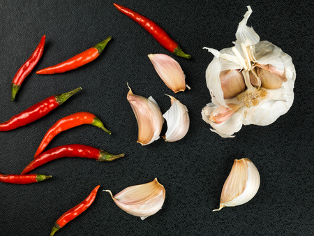 Hot Red Birds Eye Chilli and Fresh Garlic Bulbs Against a Black Backgroundの写真素材