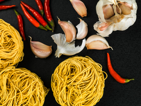 Uncooked Chinese Style Fine Egg Noodles Nests With Chilli and Garlic on a Black Backgroundの写真素材