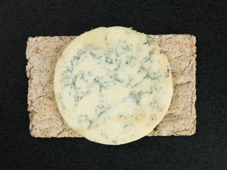 Blue Stilton Cheese on Thin Crisp Wholewheat Crackers Against a Black Backgroundの写真素材