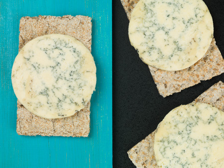 Blue Stilton Cheese on Thin Crisp Wholewheat Crackers Against a Blue and Black Backgroundの写真素材