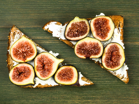 Fresh Figs and Cream Cheese on Wholegrain Toast Against a Green Backgroundの写真素材