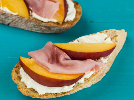 Ham and Peaches With Soft Ricotta Cheese on Ciabatta Sandwich Against a Blue Backgroundの写真素材