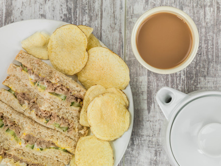 Tuna Sweetcorn and Cucumber Oatmeal Bread Sandwich With Potato Crisps Against a Distressed Wooden Backgroundの写真素材