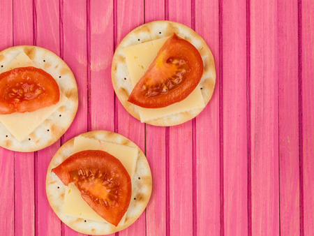Cheese and Tomato on Water Biscuit Crackers Against a Pink Wooden Backgroundの写真素材