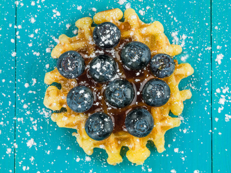Single Belgian Butter Waffle With Fresh Blueberries Against a Blue Backgroundの写真素材