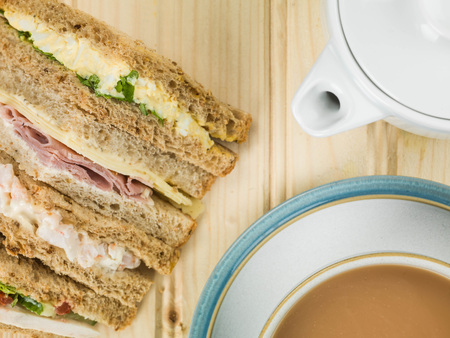 Selection of Assorted Sandwiches in Brown Bread With a Cup of Tea or Coffee Against a light Pine Wood Backgroundの写真素材