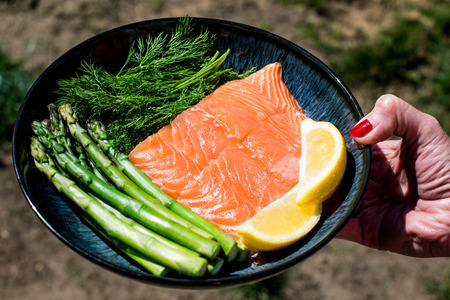 Hold a Plate of Fresh Uncooked Healthy Salmon Fillet With Asparagus Herbs and Lemonの写真素材