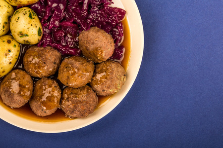 Swedish or Norwegian Meatballs With Boiled Potatoes Red Cabbage And Gravy Meal Against A Purple or Blue Backgroundの写真素材