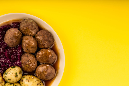 Swedish or Norwegian Meatballs With Boiled Potatoes Red Cabbage And Gravy Meal Against A Yellow Backgroundの写真素材
