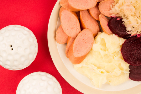 Swedish Or Norwegian Sausage With Mashed Potatoes Beetroot and Sauerkraut Meal Against A Red Backgroundの写真素材