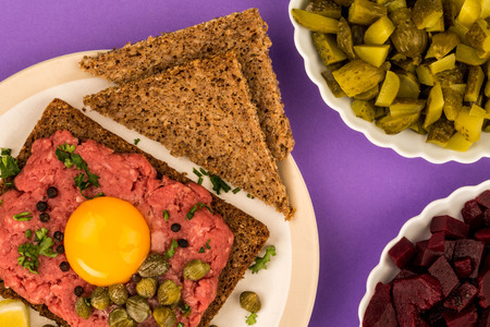Steak Tartare With Capers and A Raw Egg Open Face Sandwich Against A Purple Backgroundの写真素材