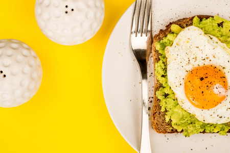 Fried Egg Sunny Side Up on Crushed Avocado And Rye Bread Open Faced Sandwich Against A Yellow Backgroundの写真素材