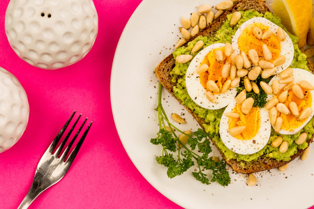 Sliced Boiled Egg on Crushed Avocado With Pine Nuts And Rye Bread Open Faced Sandwich Against A Pink Bankgroundの写真素材
