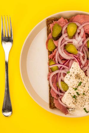Roast Beef Open Faced Sandwich With Sliced Onions Gherkins and Horseradish Sauce On Rye Bread Against A Yellow Backgroundの写真素材