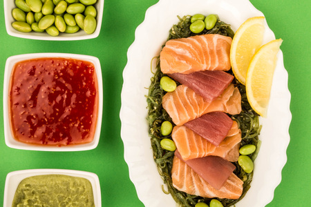 Japanese Style Slices Of Salmon and Tuna Sashimi On A Bed Of PIckled Seaweed And Edamame Beans Against A Green Backgroundの写真素材