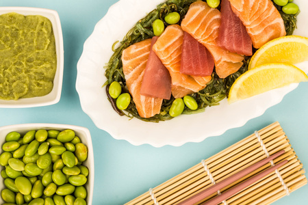 Japanese Style Slices Of Salmon and Tuna Sashimi On A Bed Of PIckled Seaweed And Edamame Beans Against A Blue Backgroundの写真素材