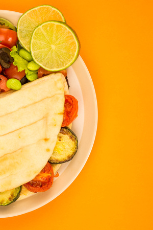 Veghetarian Style Courgette and Cherry Tomato Flatbread With A Fresh Mixed Salad Against An Orange Backgroundの写真素材