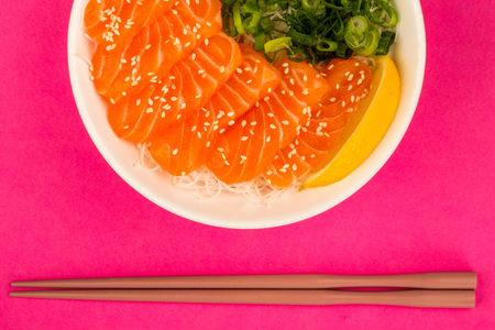 Hawaiian Poke bowl Of Salmon Sashimi With Rice Noodles And Spring Onions Against A Pink Background