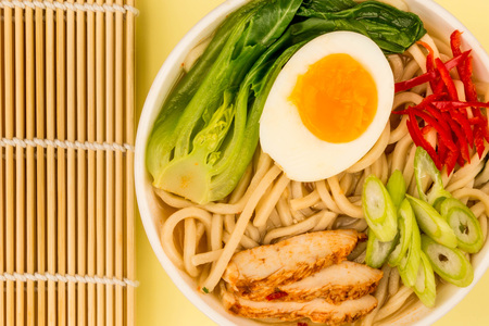 Japanese Style Chicken and Udon Noodle Broth or Soup With Pak Choi And Red Chillies Against A Pale Lemon or Yellow Backgroundの写真素材