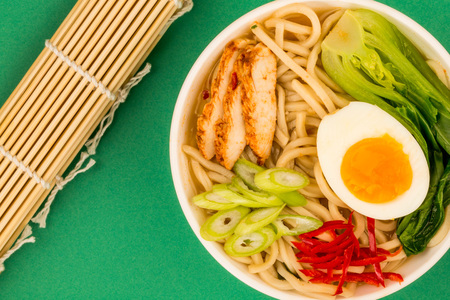 Japanese Style Chicken and Udon Noodle Broth or Soup With Pak Choi And Red Chillies Against A Green Backgroundの写真素材