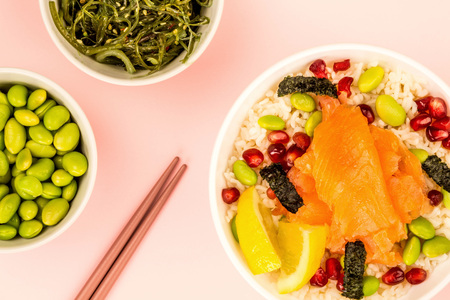 Healthy Hawaiian Style Poke Bowl Of Smoked Salmon With Rice Edamame beans Seaweed and Pomegranate Seeds Against A Pink Backgroundの写真素材