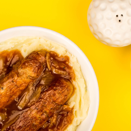 Sausage And Mashed Potatoes With Onion Gravy Against A Yellow Backgroundの写真素材